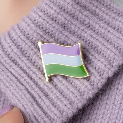 Close-up of a genderqueer pride flag enamel pin on a lavender knitted fabric