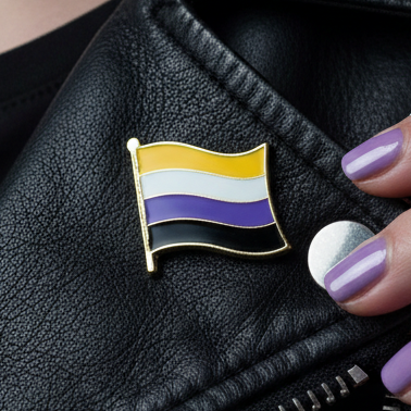 Close-up of the Non-Binary Flag Enamel Pin, featuring yellow, white, purple, and black stripes, on a black leather jacket lapel. A hand with purple nails holds the backing beside it.