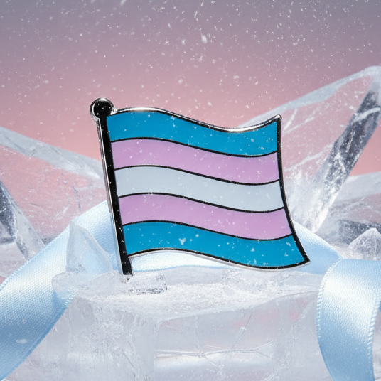 Trans flag enamel pin displayed upright on an icy block with pale blue ribbons