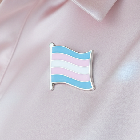 Close-up of a trans pride flag enamel pin on pale pink fabric
