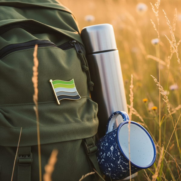 Aromantic pride flag enamel pin on a green backpack beside a stainless-steel bottle