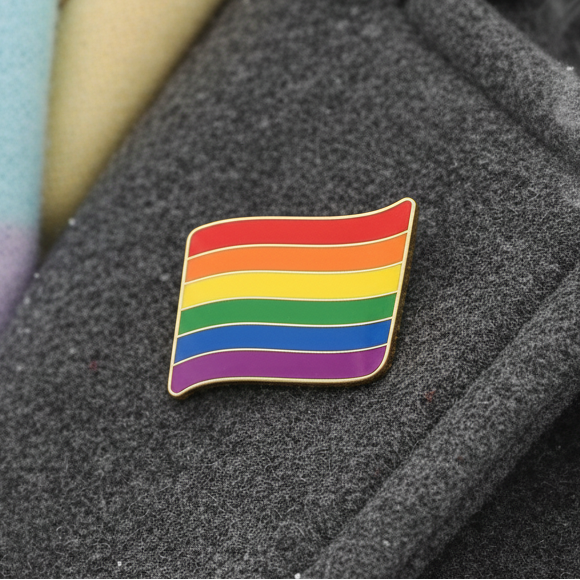 Rainbow LGBT flag enamel pin resting on dark textured fabric