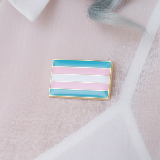 Trans pride enamel pin with blue, pink, and white horizontal stripes on pink fabric