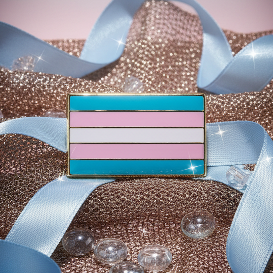 Trans Pride Enamel Pin, featuring the transgender-pride flag's vibrant stripes, displayed on a sparkly rose-gold background with decorative pale blue ribbon and clear glass pebbles, embodying bold queer visibility and self-expression.