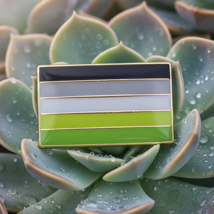 Aromantic pride enamel pin with black, gray, white, and green stripes on a dewy succulent
