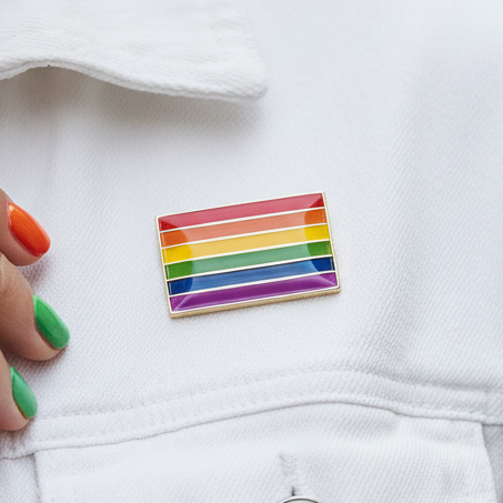 Rainbow LGBT Pride enamel pin resting on white clothing, with a hand-painted rainbow manicure
