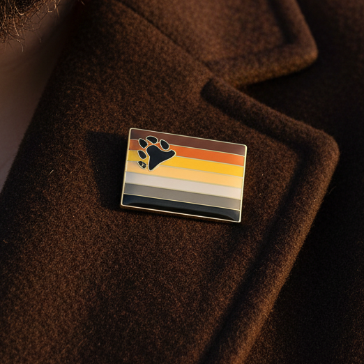 Bear Pride Enamel Pin on a brown coat, featuring bear pride flag colors with a black bear-paw. A vibrant accessory celebrating LGBTQIA+ pride and self-expression. Perfect for showcasing fierce, inclusive queer identity.