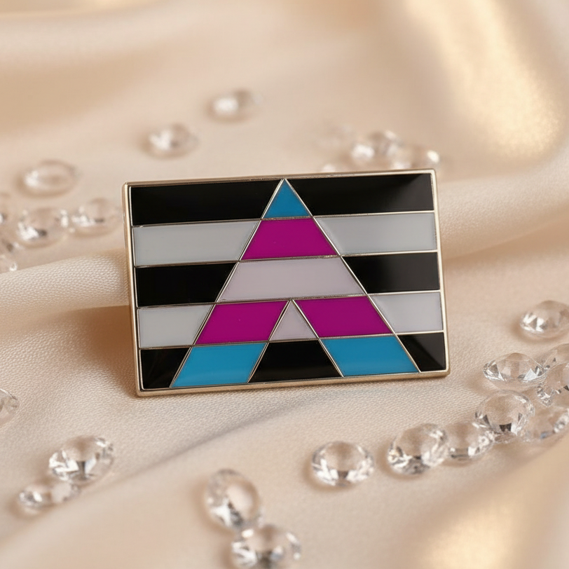 Trans Ally Enamel Pin on champagne satin, featuring black and white bars with a stylized A in transgender pride colors, surrounded by sparkling gems, celebrating bold self-expression and LGBTQIA+ pride.