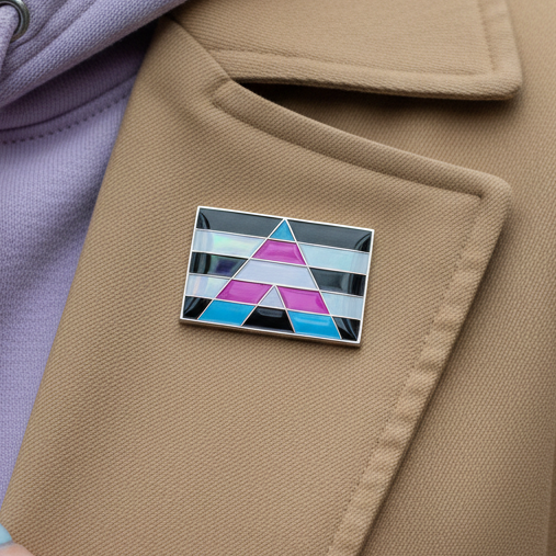 Trans Ally Enamel Pin on a camel-colored coat, showcasing a bold geometric A in vibrant stripes, symbolizing pride and empowerment. A lilac garment peeks underneath, enhancing the pin's vibrant expression.