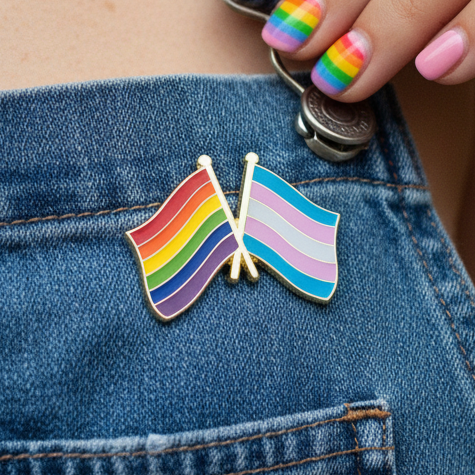 Close-up of One Community Together - Trans + LGBT Flag Enamel Pin on denim, with a rainbow-gradient manicure, celebrating unity, visibility, and pride in queer self-expression and mutual support for LGBTQIA+ and transgender communities.