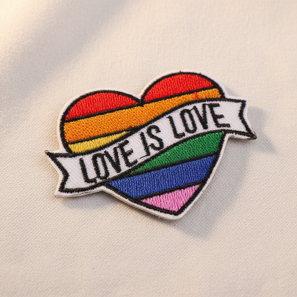 Embroidered rainbow heart patch with a white banner reading “LOVE IS LOVE”