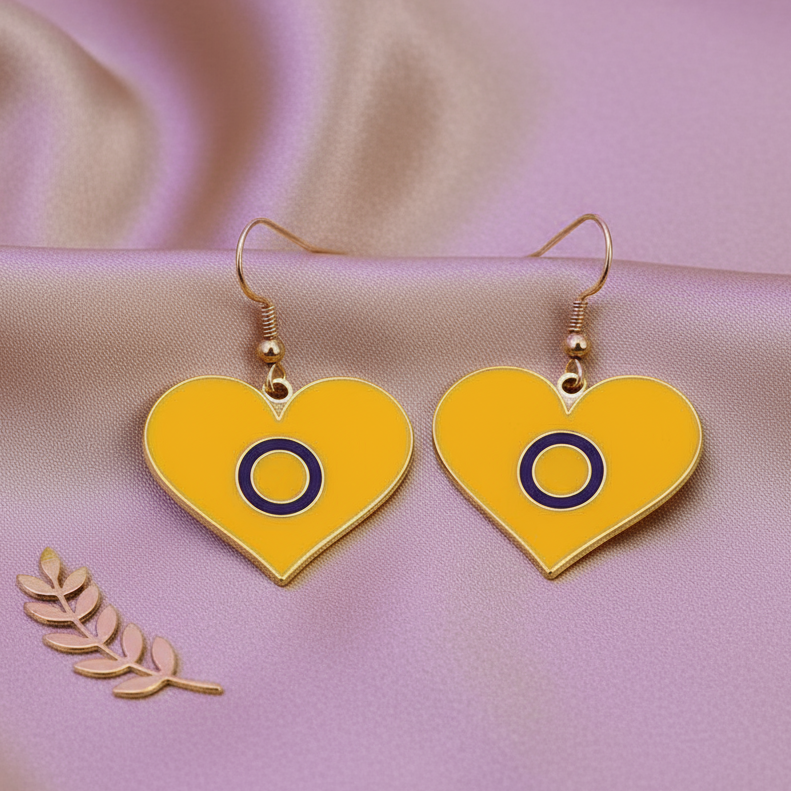 Yellow heart earrings with purple-ring symbols on gold-tone hooks, arranged on pink fabric