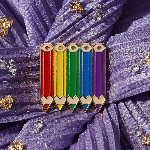 Close-up rainbow enamel pin shaped like five sharpened colored pencils