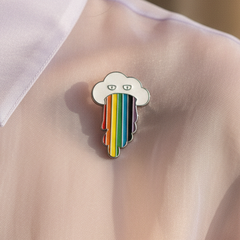Rainbow cloud enamel pin with rainbow-striped raindrops on pale pink fabric
