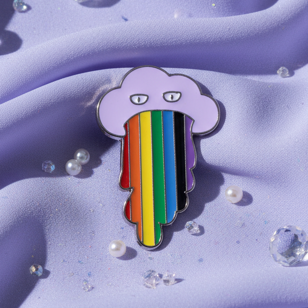 Rainbow Cloud Enamel Pin featuring a lavender cloud with pride flag drips, resting on lilac fabric adorned with pearls and beads, symbolizing empowerment and joyful queer self-expression.