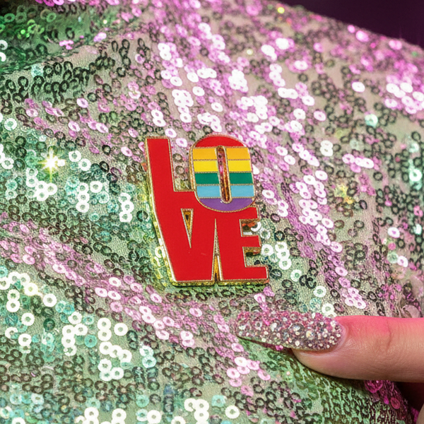 LOVE enamel pin with a rainbow-striped heart, shown on iridescent sequin fabric