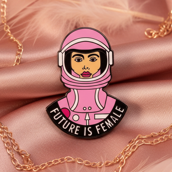 Pink astronaut woman enamel pin reading “FUTURE IS FEMALE” on satin with gold chains