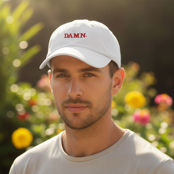 Close-up of a person wearing a white baseball cap embroidered with red “DAMN.” lettering