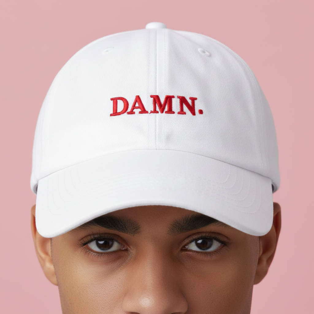 Model wearing a white baseball cap embroidered with red “DAMN.” lettering