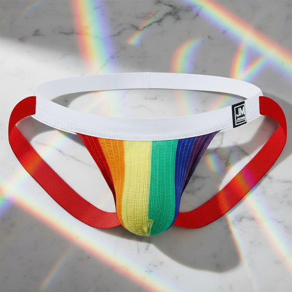 Jockmail LGBT Pride Jockstrap with rainbow-striped pouch, white waistband, and red leg straps, laid flat on marble. Breathable polyester/spandex blend celebrates pride, visibility, and self-expression with bold queer energy.