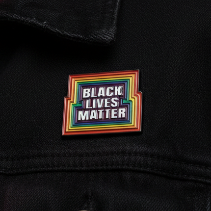 Rainbow-bordered “BLACK LIVES MATTER” enamel pin on black fabric