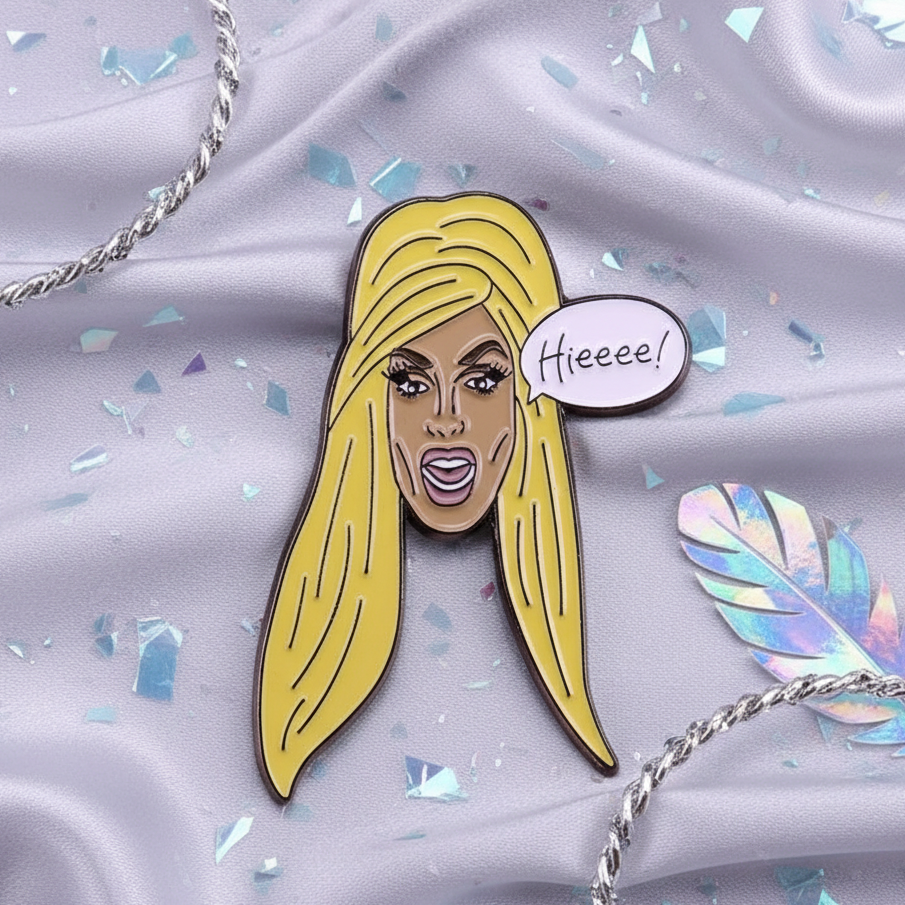 Enamel pin of a blonde drag performer with a “Hieeee!” speech bubble