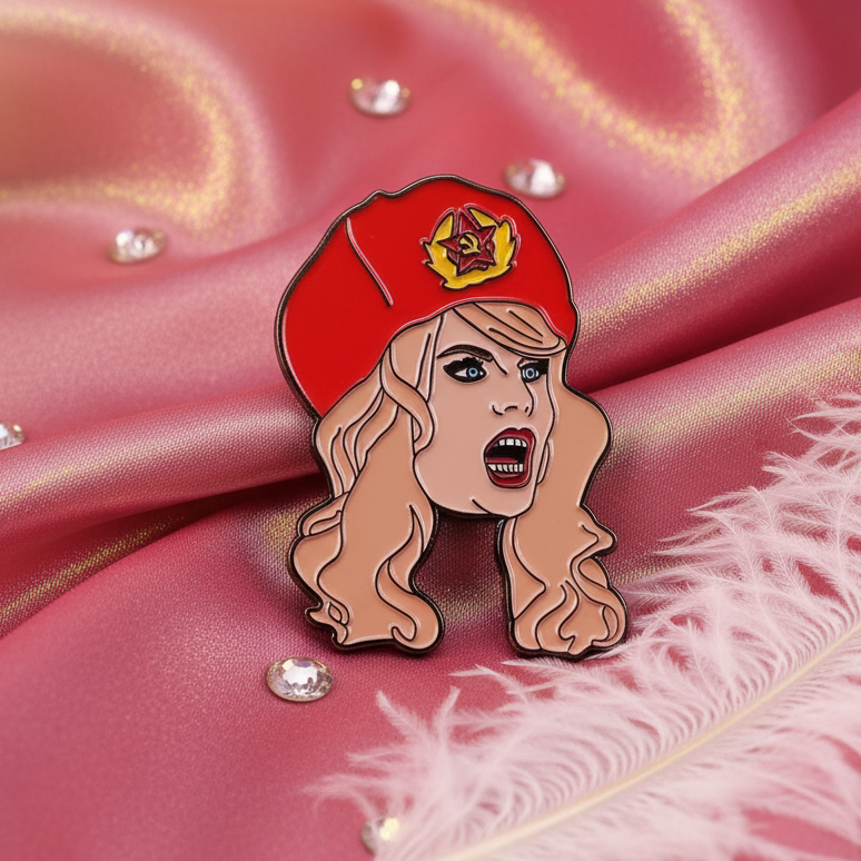 Katya Zamolodchikova Enamel Pin on pink satin, featuring a pop-art woman's face with blond hair and a red beret, symbolizing bold queer pride and vibrant self-expression.