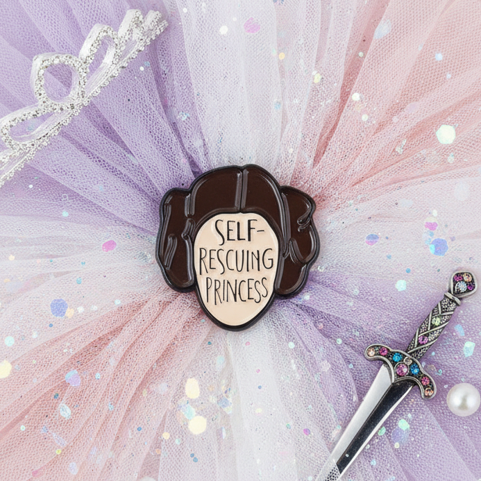 Self-Rescuing Princess enamel pin with a dark-haired profile and cream text panel