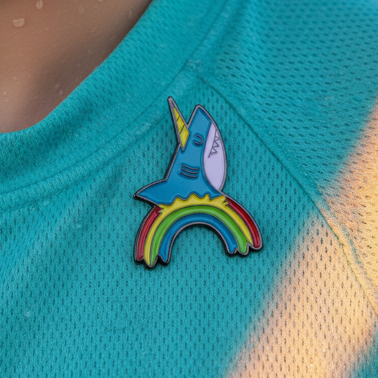 Close-up of a rainbow shark enamel pin attached to a turquoise mesh shirt