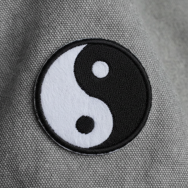 Black-and-white yin-yang embroidered iron-on patch shown close up on gray fabric