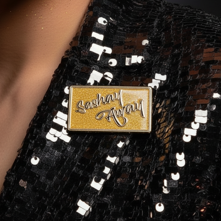 Close-up of a gold “Sashay Away” enamel pin on a black sequined garment