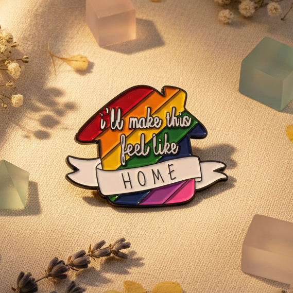 Rainbow enamel pin reading “I'll make this feel like HOME” on a banner