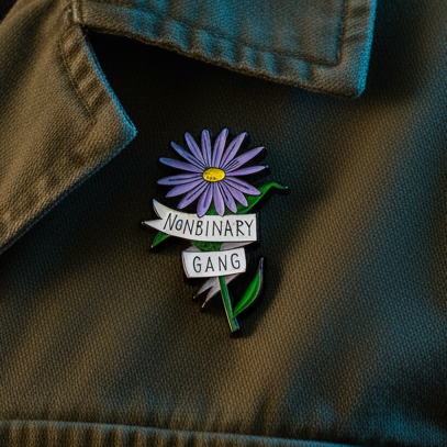 Nonbinary Gang enamel pin with purple flower and white text on a dark jacket