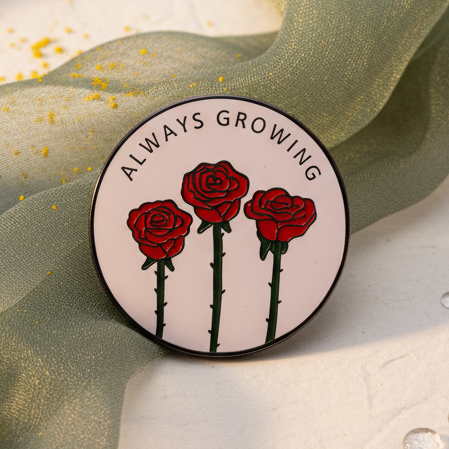 Close-up of a round enamel pin reading “ALWAYS GROWING” above three red roses