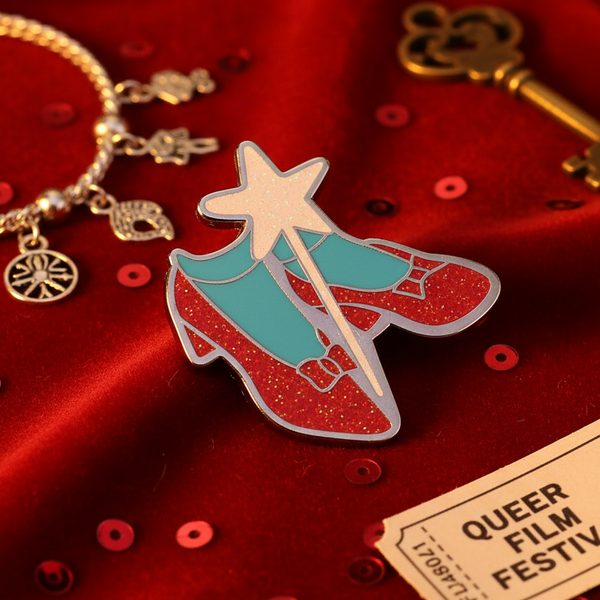 Ruby slipper enamel pin with glittery red shoes and turquoise accents on red fabric