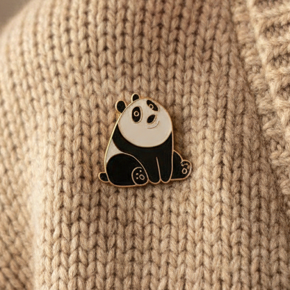 Black-and-white panda enamel pin displayed on a beige knitted sweater