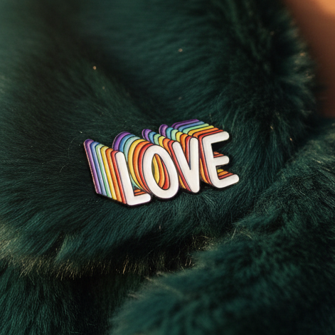 Rainbow-striped LOVE enamel pin resting on dark green furry fabric
