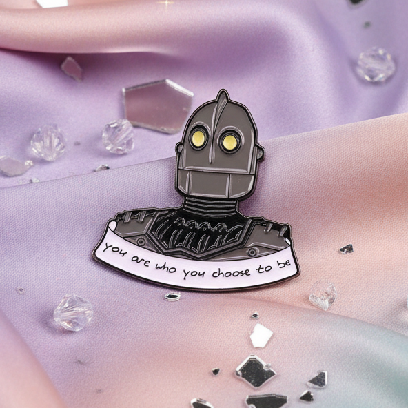 Robot enamel pin reading “You are who you choose to be” on pastel fabric