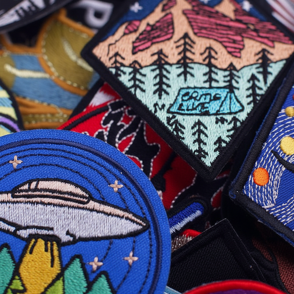 Set of 30 embroidered iron-on patches with dinosaur, UFO, star and planet designs in a beige fabric pouch