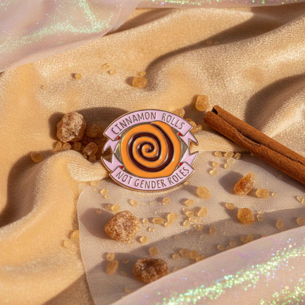 Cinnamon Rolls Not Gender Roles enamel pin on shimmering fabric with cinnamon sticks and crumbs