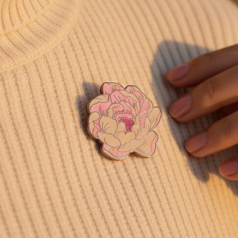 Pastel pink flower blooming enamel pin on ribbed fabric beside a hand