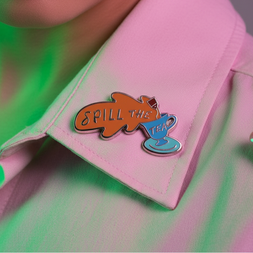 Spill the Tea enamel pin shaped like an orange tea bag and blue teacup