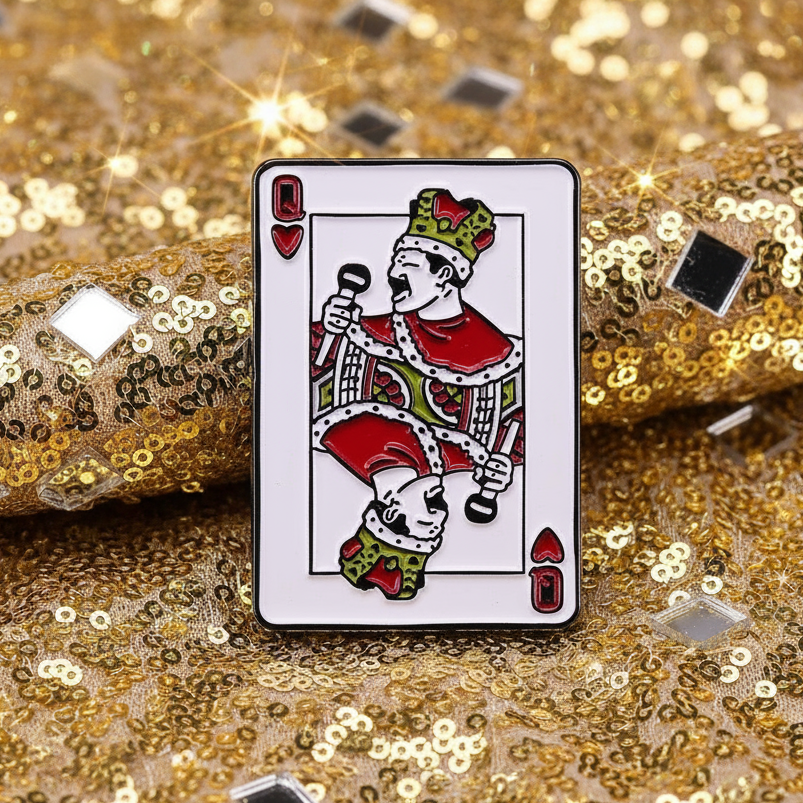 Queen Freddie Enamel Pin, a vibrant enamel pin inspired by the Queen of Hearts, rests on a dazzling gold fabric, embodying bold queer pride and stylish self-expression for the LGBTQIA+ community.