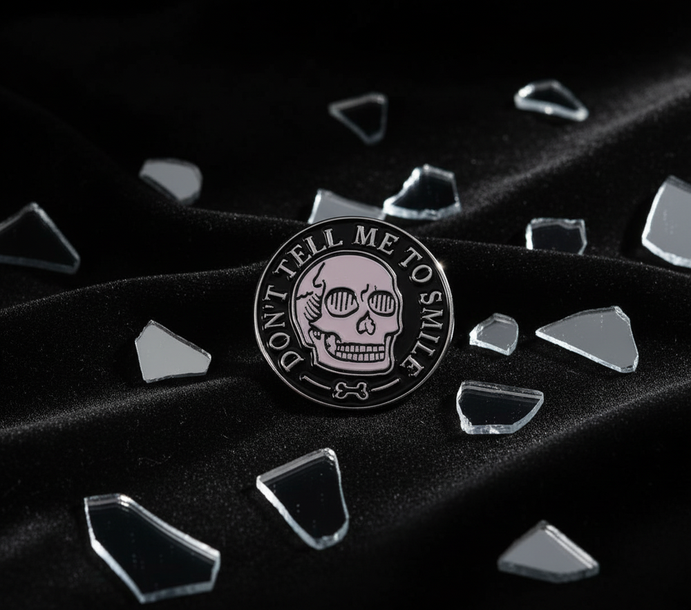 Close-up enamel pin reading “DON’T TELL ME TO SMILE,” with a skull on black fabric