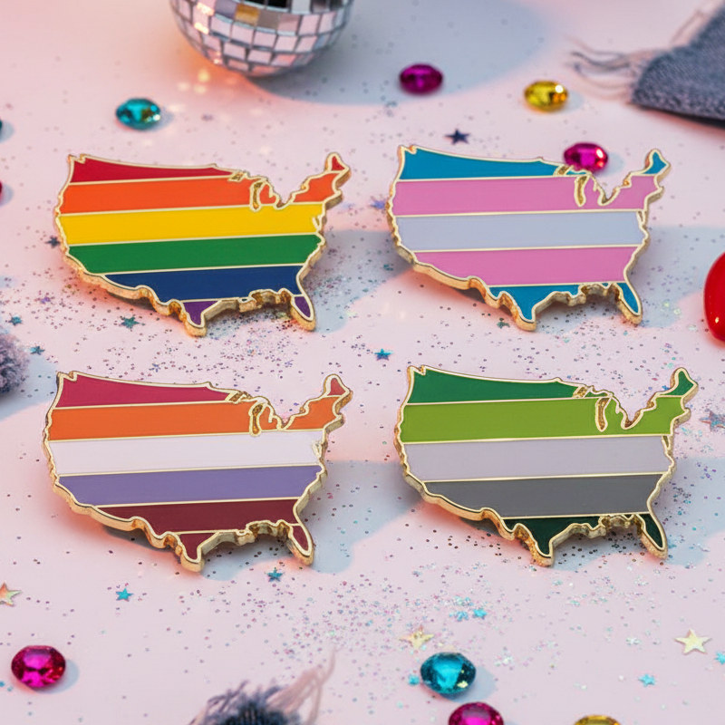 Queer USA Enamel Pins showcasing LGBTQ+, Trans, Lesbian, and Aromantic pride flags in the U.S. shape, set on a sparkling surface, reflecting bold, inclusive self-expression and vibrant queer visibility.