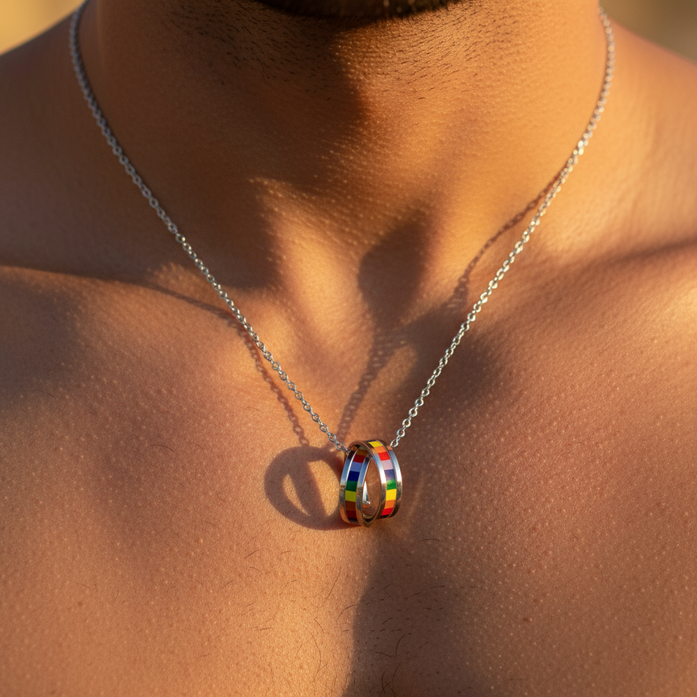 Close-up of a silver chain necklace with two interlocking rainbow-striped rings on a bare chest