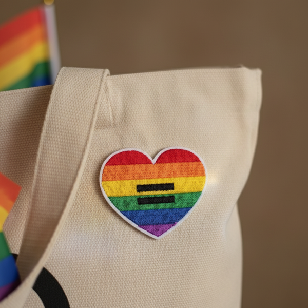 Embroidered rainbow heart patch with two black equal signs on a beige canvas bag
