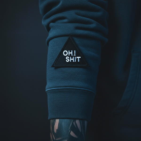 Black triangular embroidered “OH! SHIT” iron-on patch shown on a dark sleeve