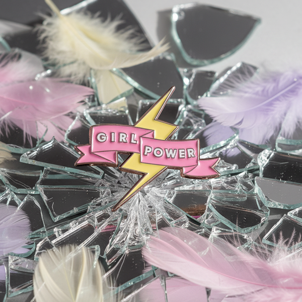Close-up of a pink and yellow Girl Power lightning-bolt enamel pin on broken glass and feathers