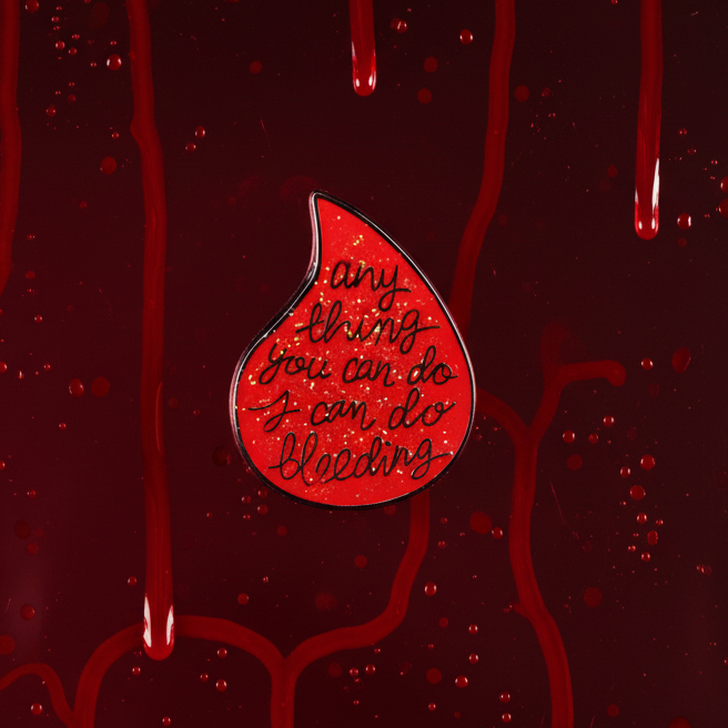 Red teardrop enamel pin reading “anything you can do I can do bleeding” on a blood-red background